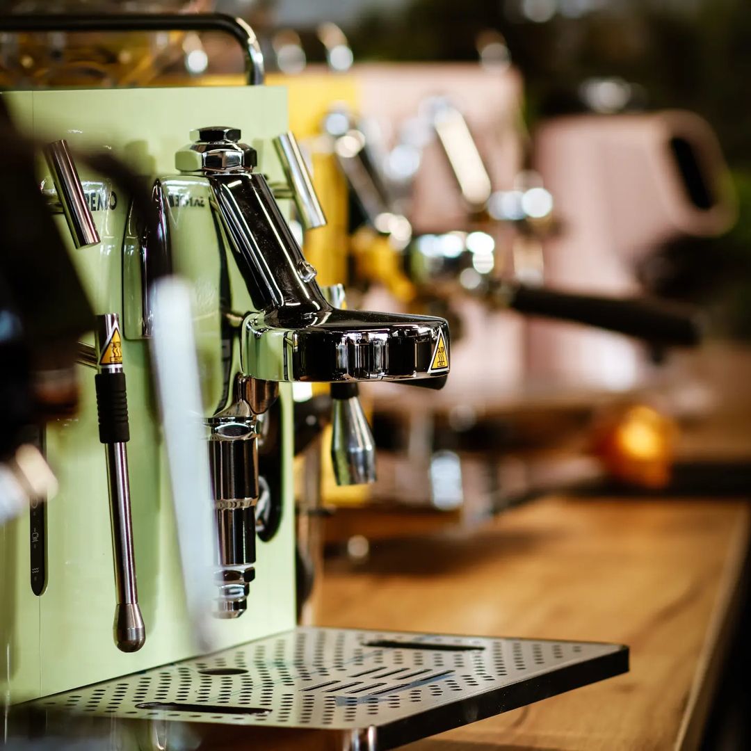 Close-up of Sanremo espresso machines in vibrant colors on a wooden counter, chrome grouphead and steam wand highlighting Italian design and craftsmanship.
