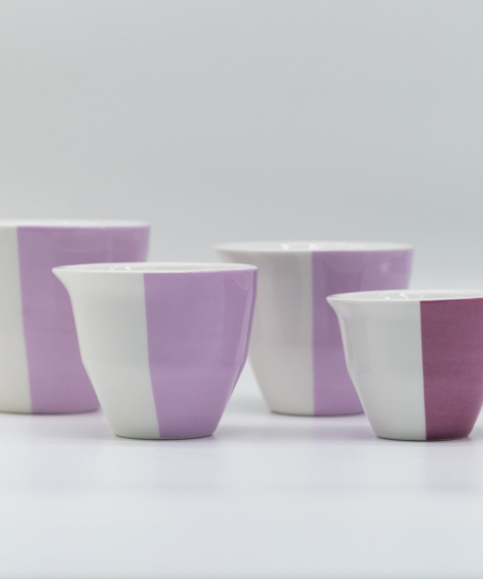 Four ceramic cups with purple and white striped design on a light gray background