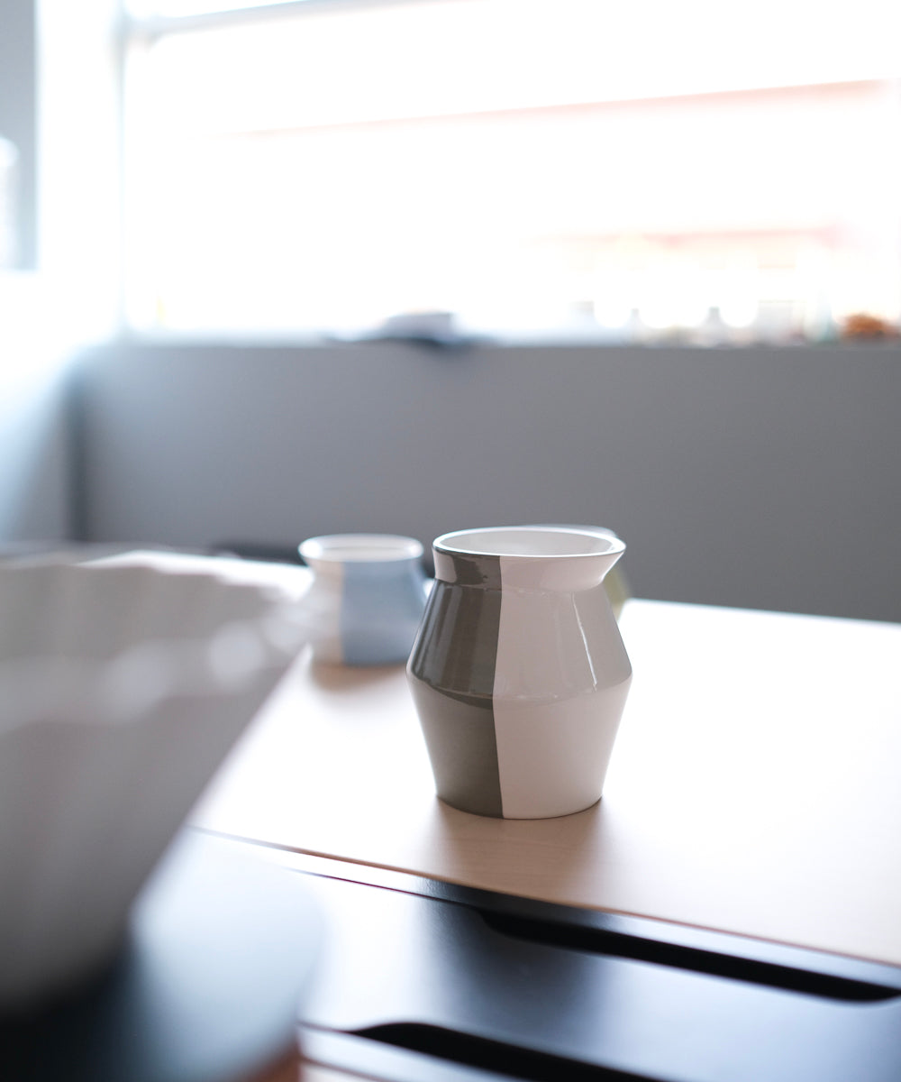 2-WayCup Refined Version 330ml grey cup and 130ml blue cup sitting on the edge on a counter or desk with a window in the background