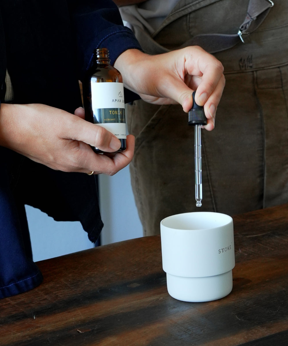 APAX Lab Water Minerals Tonik Bottle shown being held in one hand of female with other hand holding dropper dripping into cup standing next to a male