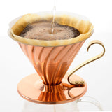 Copper coffee dripper with coffee being poured into it on a white background