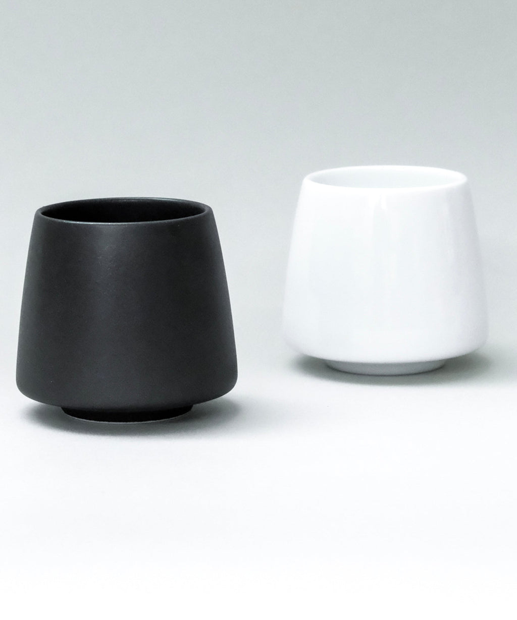 Two origami aroma ceramic flavor cups, one black and one white, on a light gray background