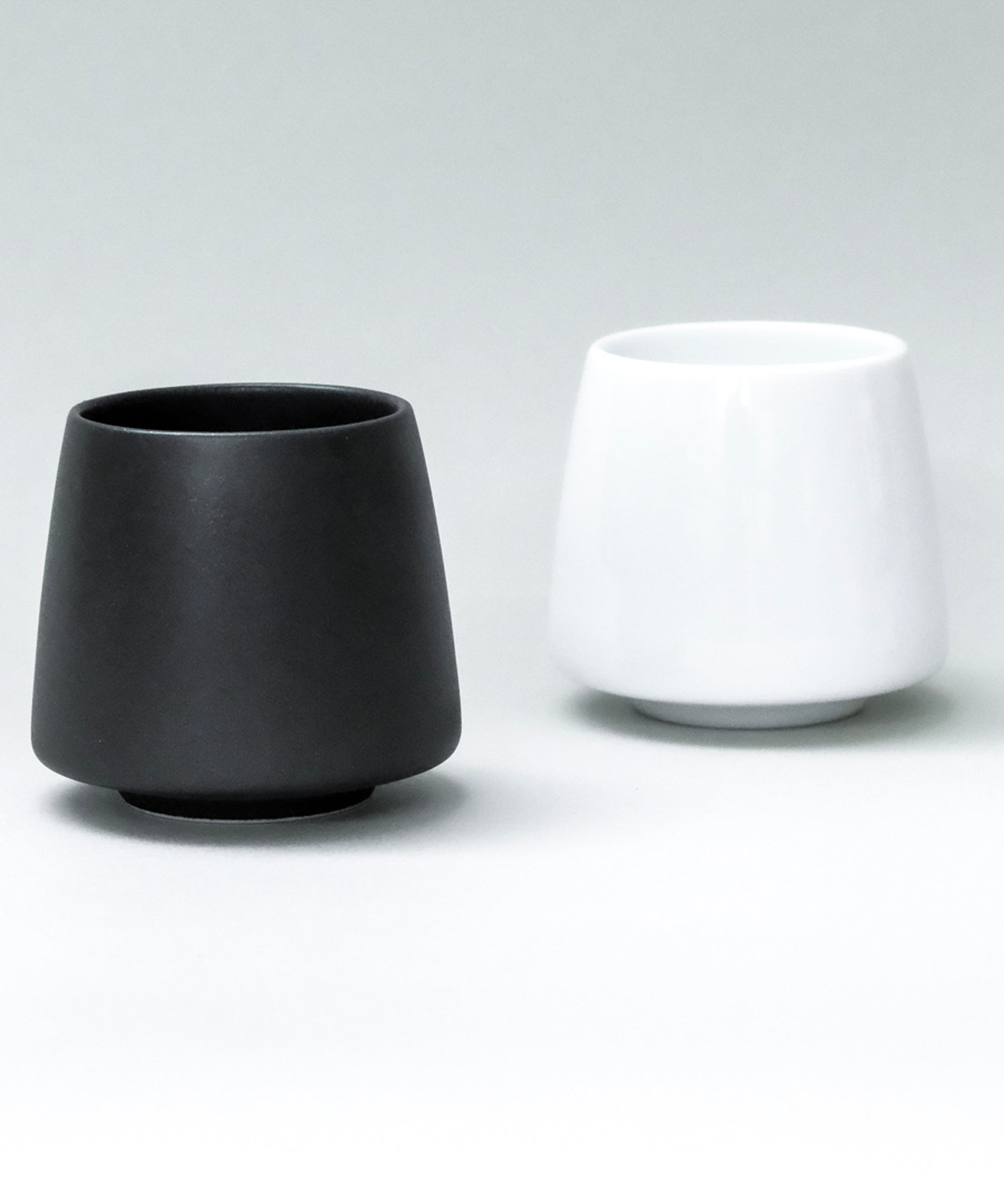 Two origami aroma ceramic flavor cups, one black and one white, on a light gray background