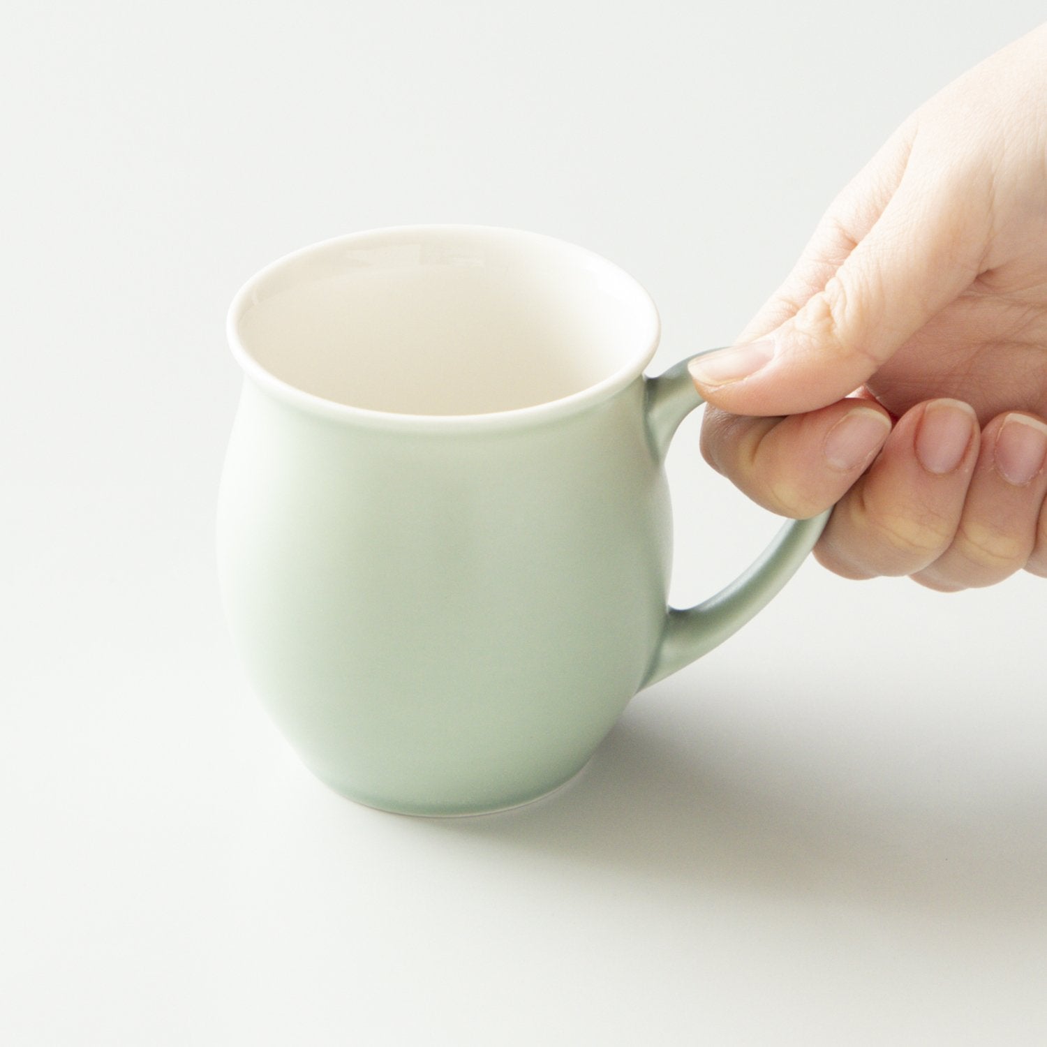 Hand holding a light green mug on a white background