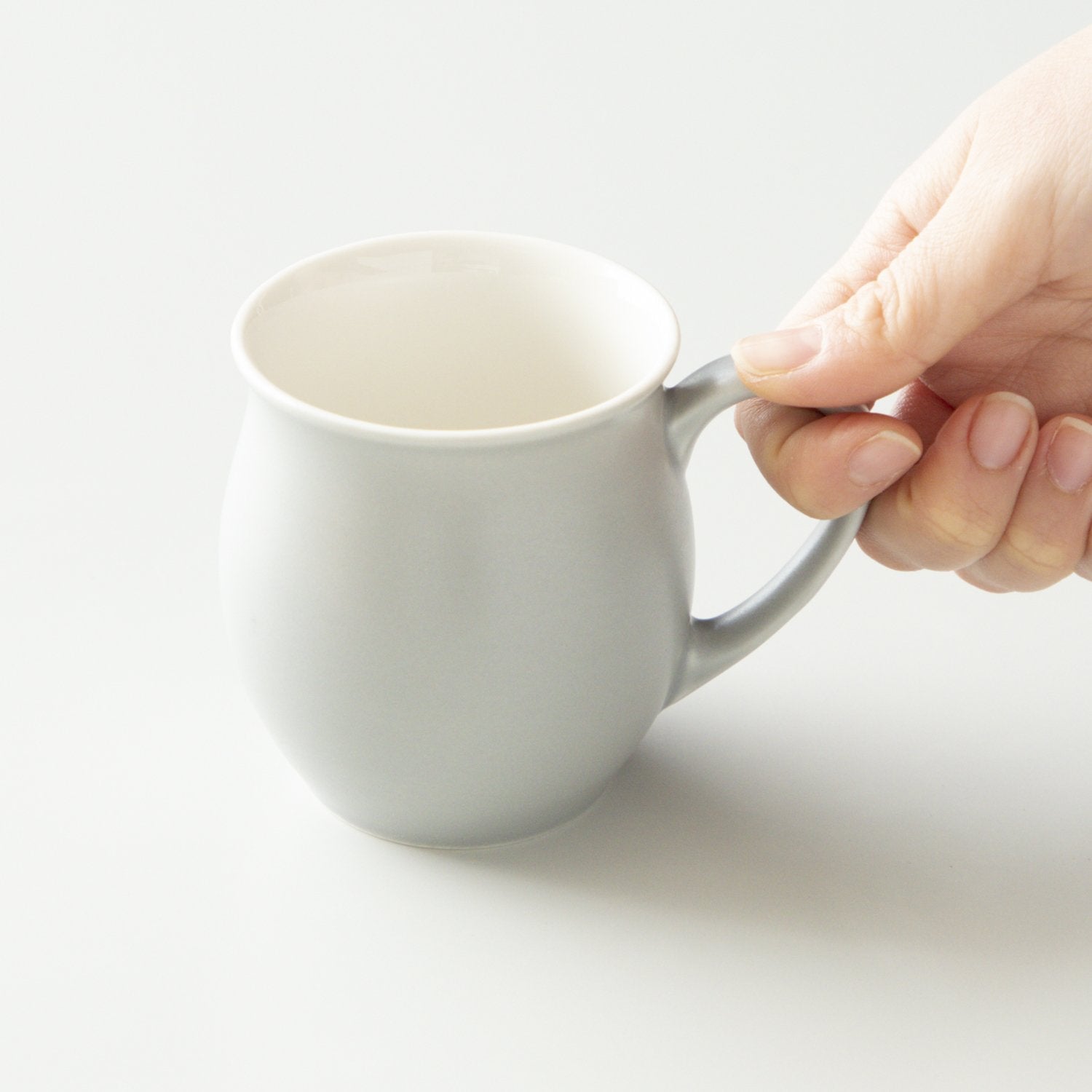 Grey mug held by a hand on a light background