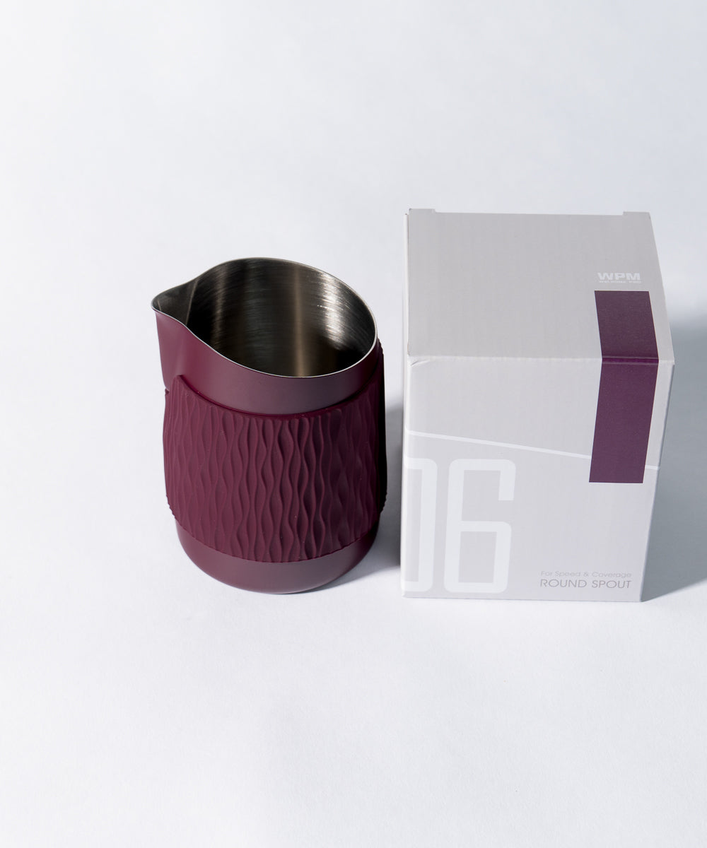 WPM Pitcher in Aubergine shown from the side, featuring a sleek handleless design for latte art pictured with the packaging box