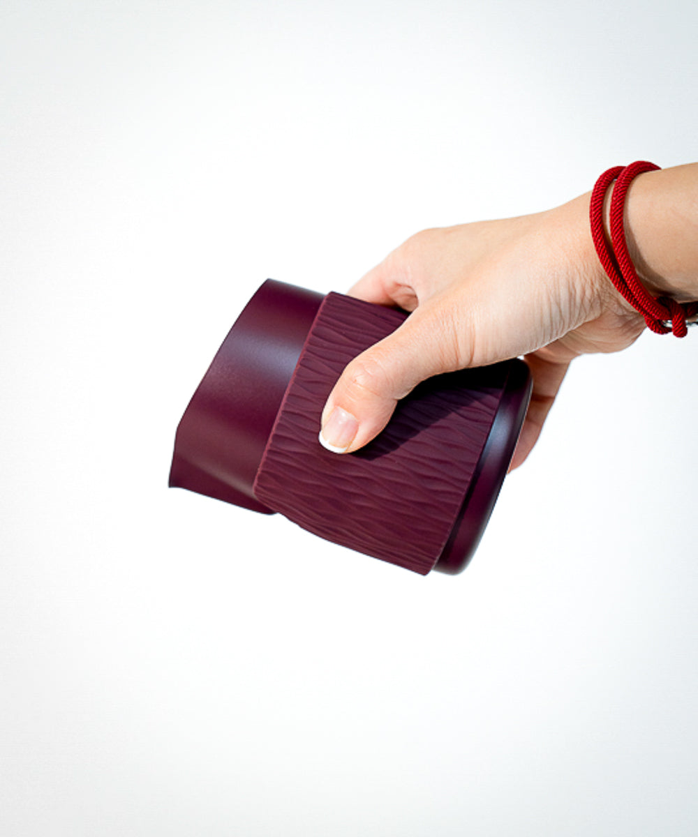 Hand holding a maroon latte art milk pitcher against a white background