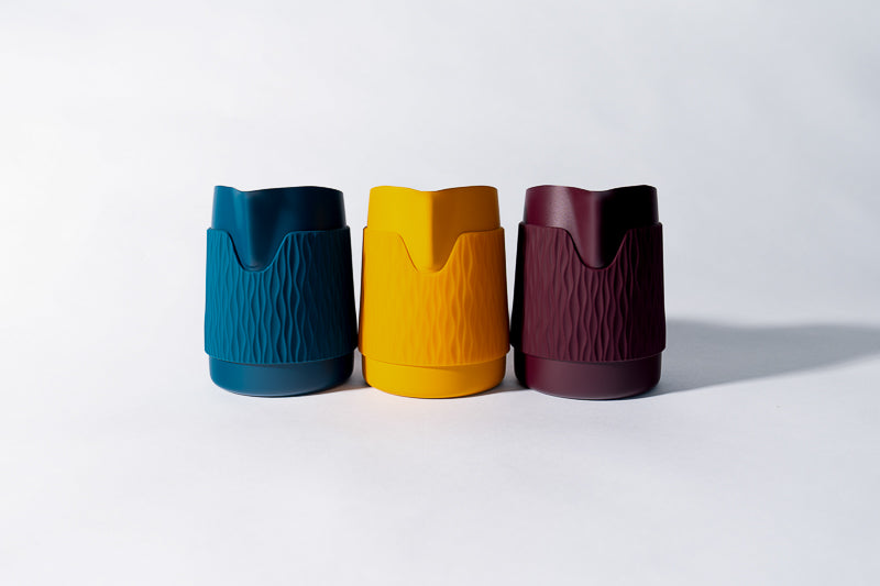 Three colorful latte art pitchers in blue, yellow, and red on a white background