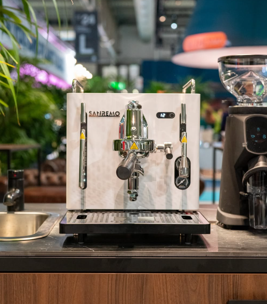 Sanremo CUBE A R white home espresso coffee machine on a counter in a commercial space with plants with blurred background