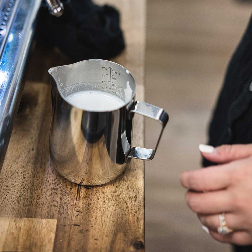 Metal pitcher with milk on a wooden surface, blurred background